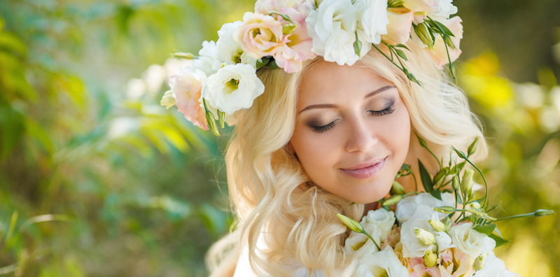 Blue-eyed bride with a beautiful blond ,curly,long hair in a white wedding dress and a beautiful wreath of pink and white roses,swinging on a swing decorated with flowers rose in the summer outdoors in the Park.